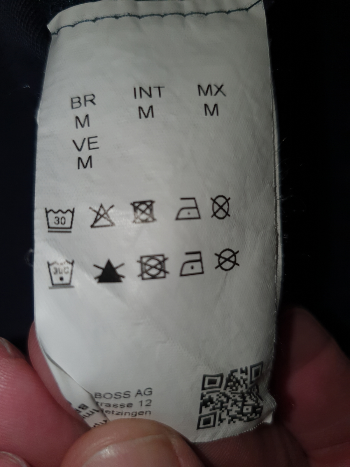 Clothing care label showing size M, washing symbols, and QR code for men's fashion
