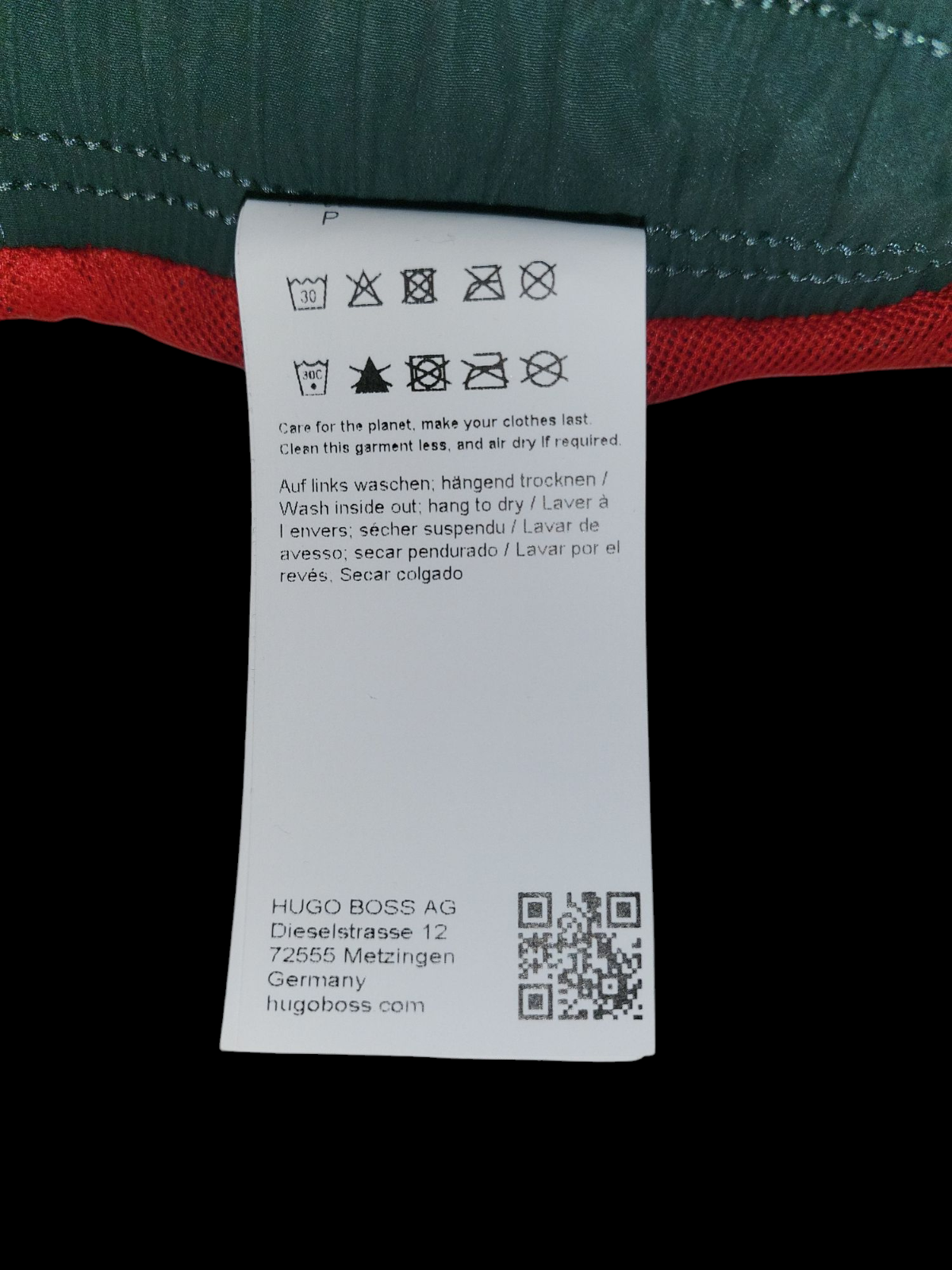 Men's designer clothing care label with washing instructions and green red fabric background