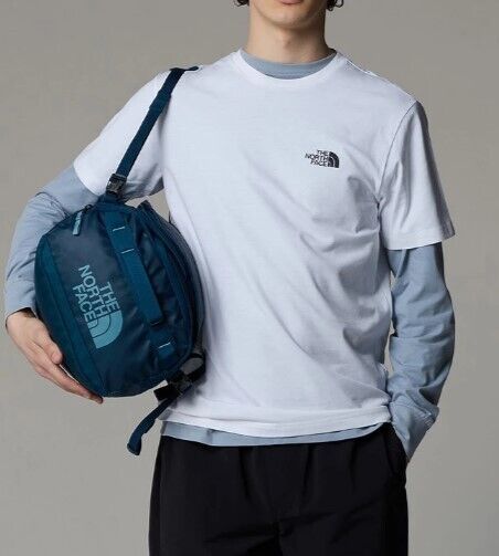 Man wearing white The North Face t-shirt, blue long sleeve, black pants, holding blue logo duffel bag