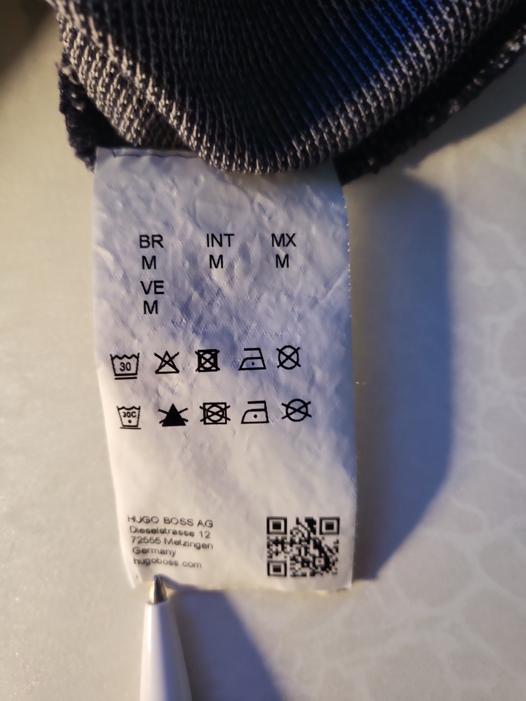 Clothing care label with washing symbols and medium size info on a textured fabric garment